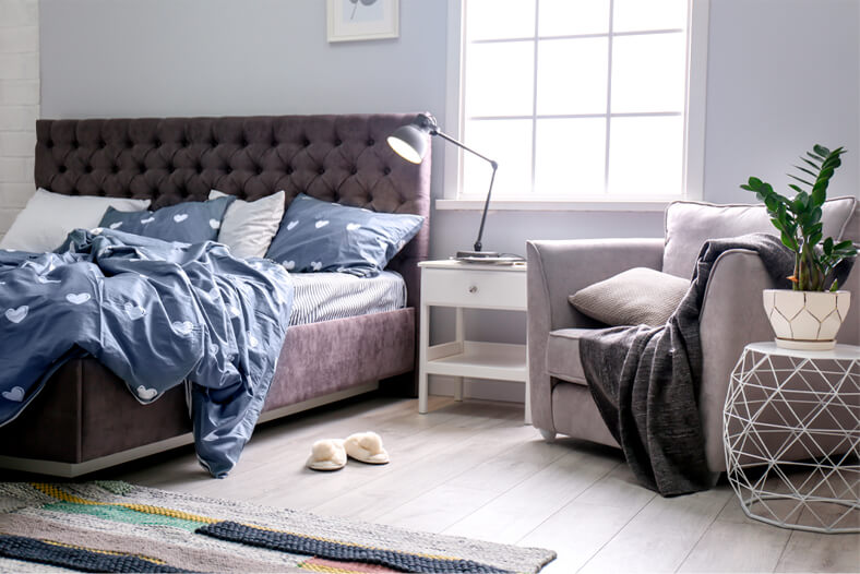 Light grey armchair in cosy, neutral bedroom with grey bed and headboard with white and blue bedding